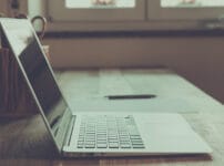 Microsoft 365のライセンス（サブスクリプション）更新作業を行うノートパソコンのイメージ。デスク上にPCと筆記具が置かれた落ち着いた作業環境。
