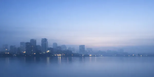 静かな夜明け前の青灰色の都市風景。穏やかな空とぼんやりしたビルのシルエットが広がる、落ち着いた雰囲気のプロフィール背景画像